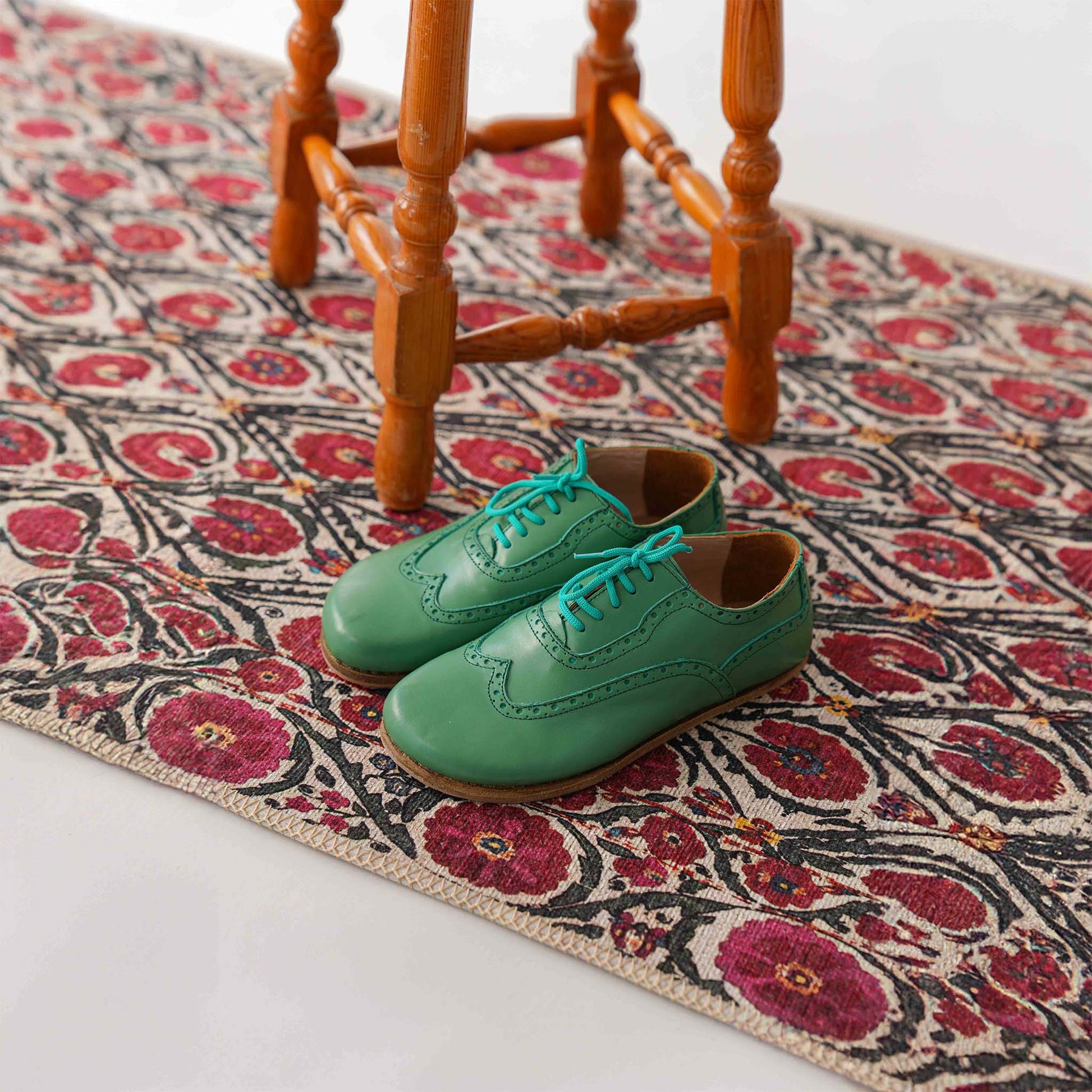 Green Doris Leather Barefoot Women Oxfords with teal laces, displayed on a patterned rug near a wooden stool.