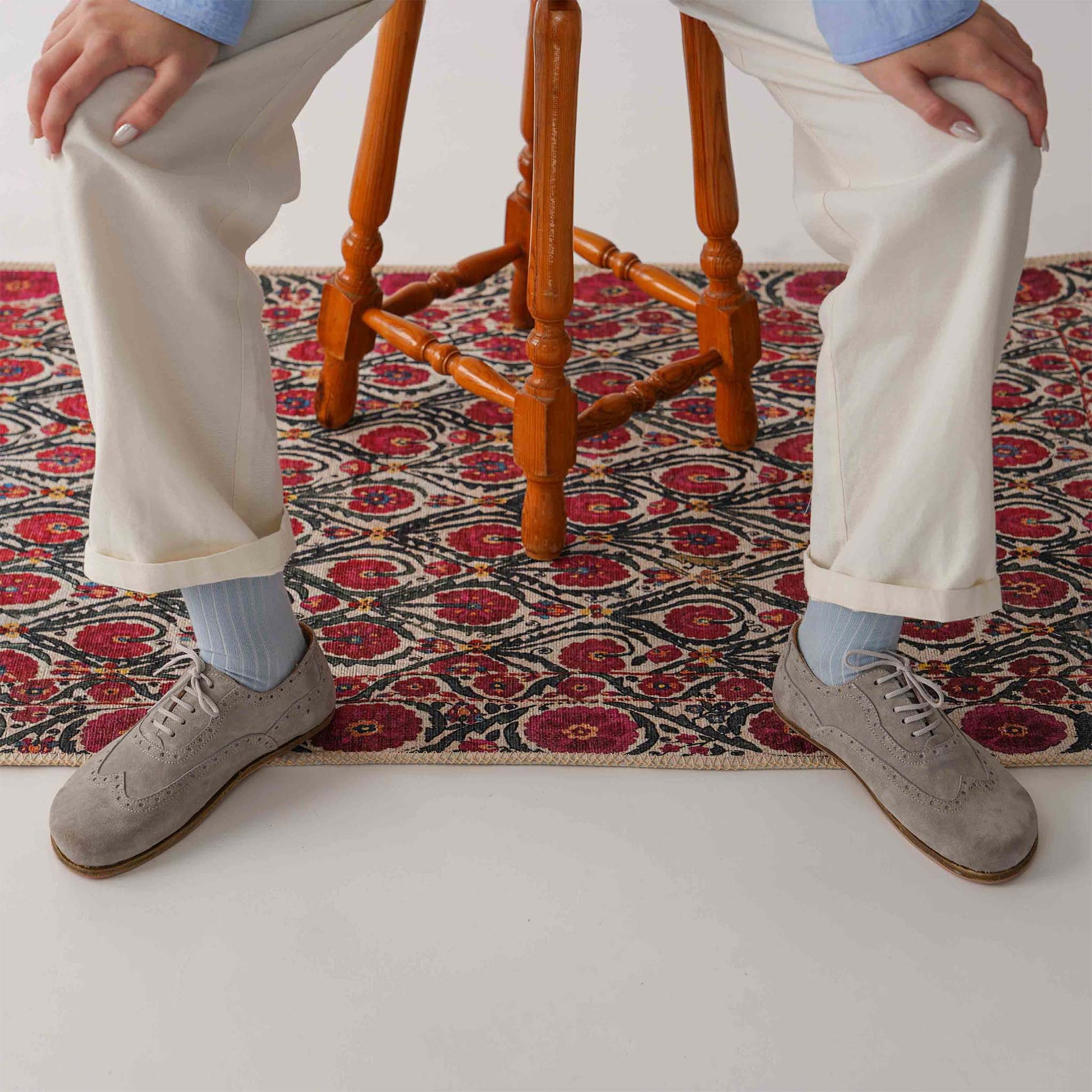 Model seated on a colorful rug, wearing gray Doris leather barefoot women Oxfords paired with white pants and blue socks.