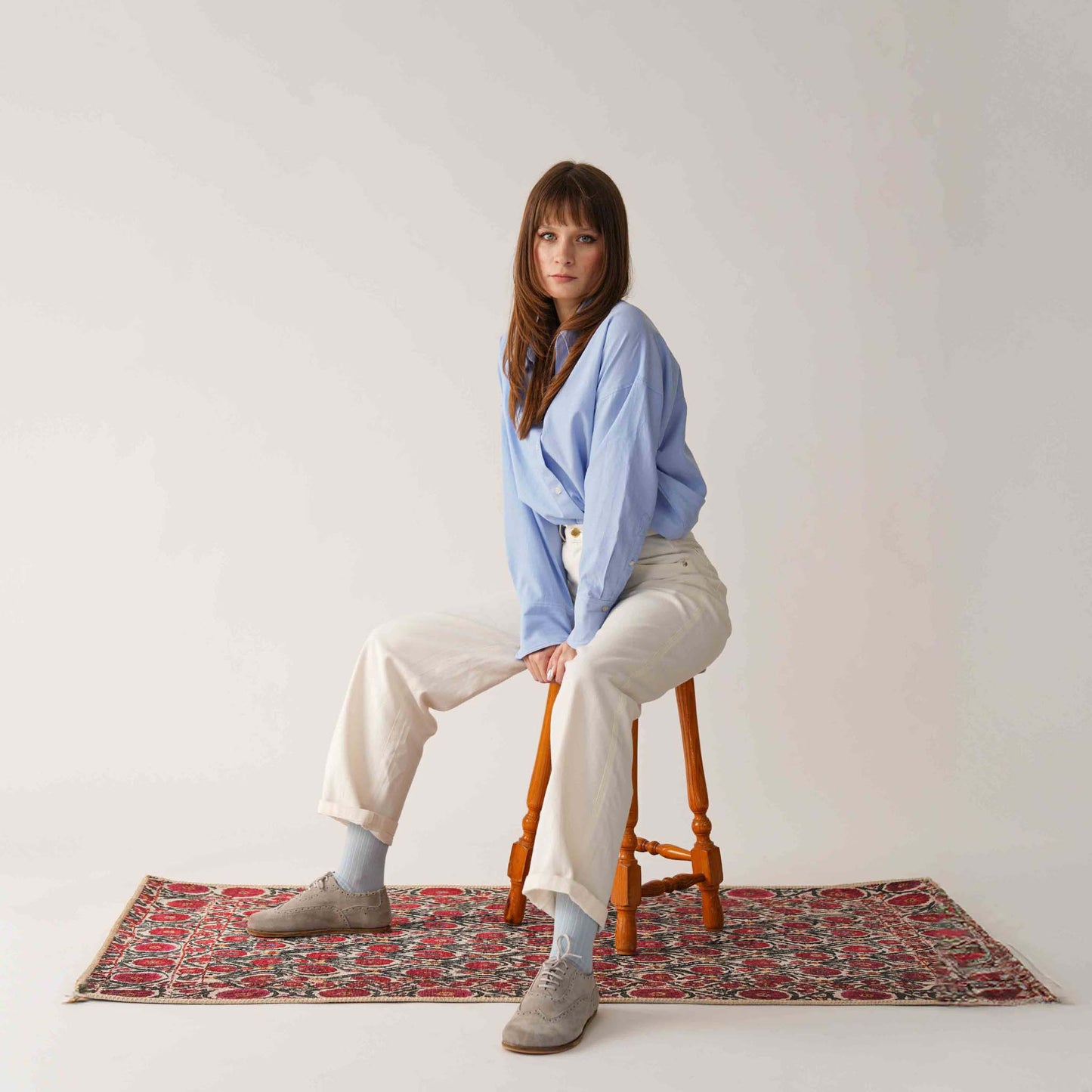 Model wearing gray Doris leather barefoot women's oxfords, sitting on a wooden stool on a patterned rug.
