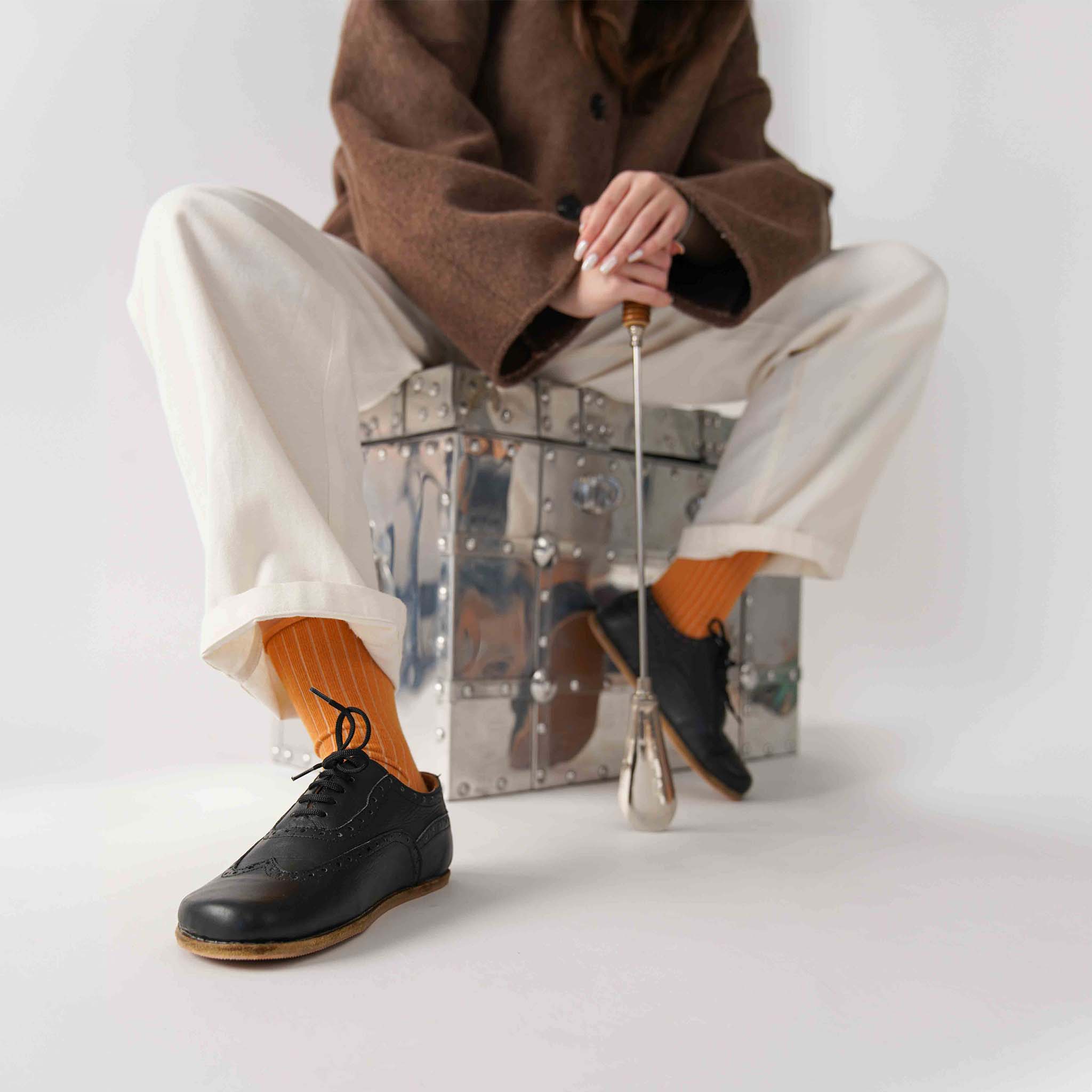Doris Leather Barefoot Women's Oxfords in Black, worn by a model sitting on a metallic chest