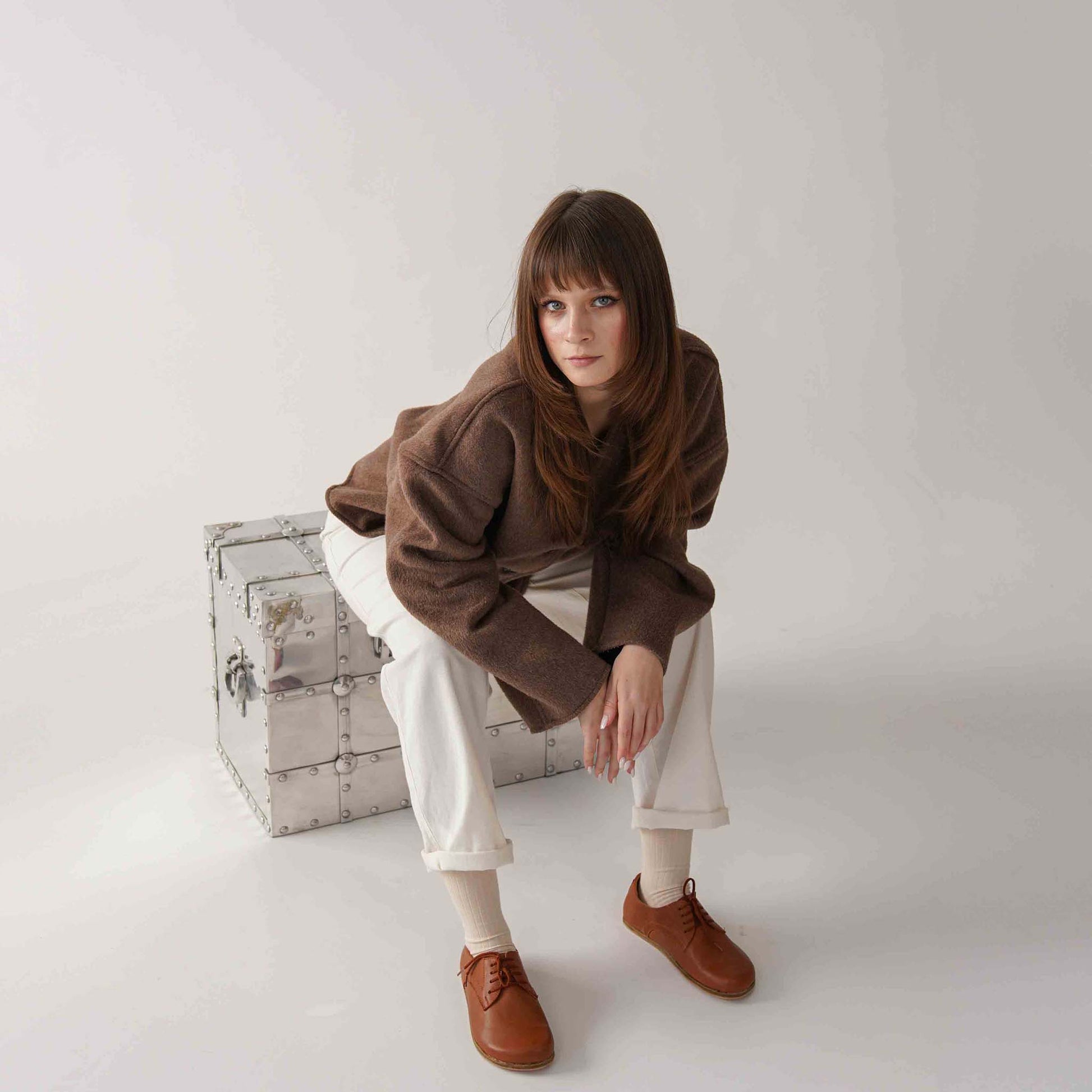 Model sitting in a stylish outfit, wearing Locris Tan Brown Leather Barefoot Women Oxfords, highlighting comfort and versatility.