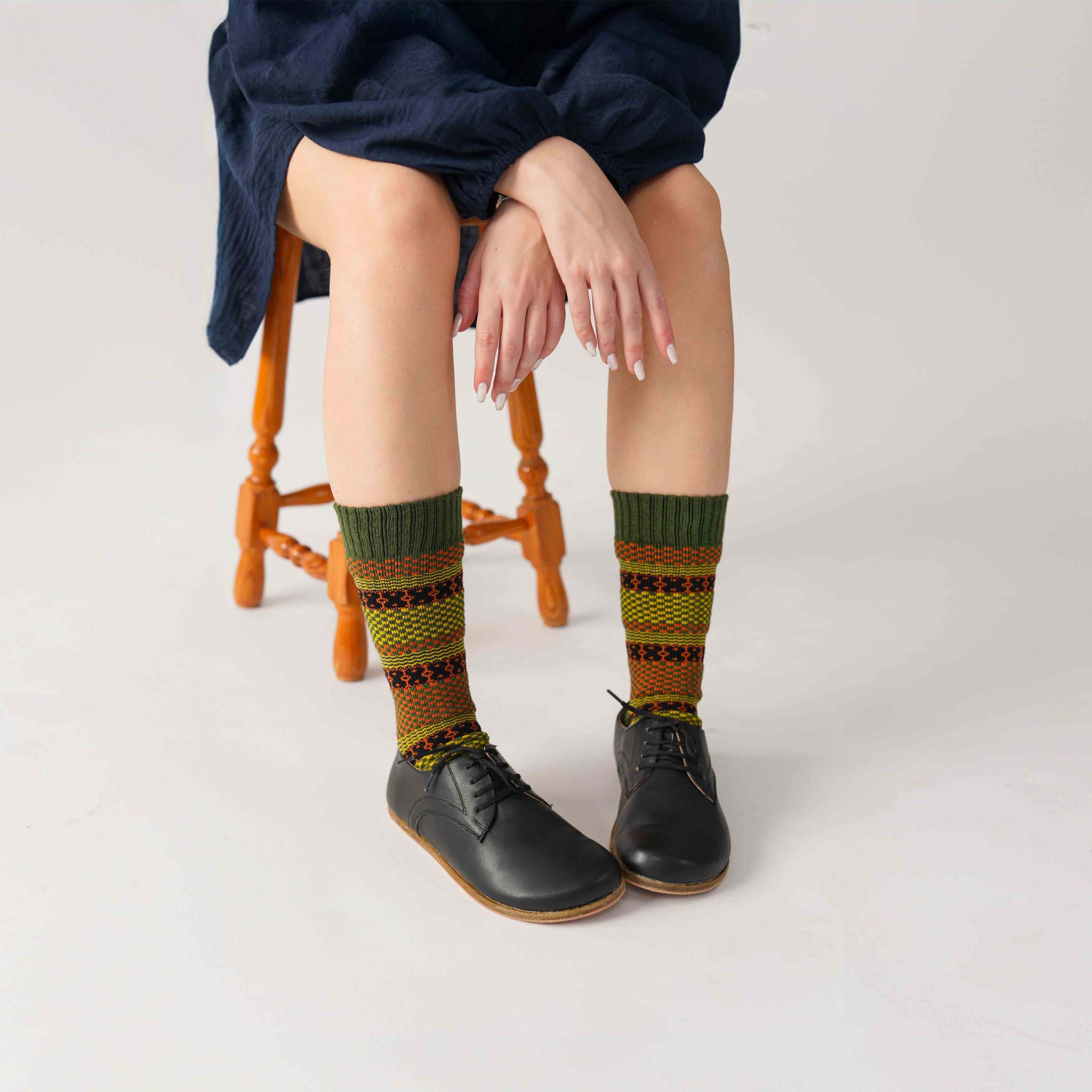 Model sitting on a stool, wearing black Locris Leather Barefoot Women Oxfords with colorful socks, demonstrating the stylish and relaxed look.