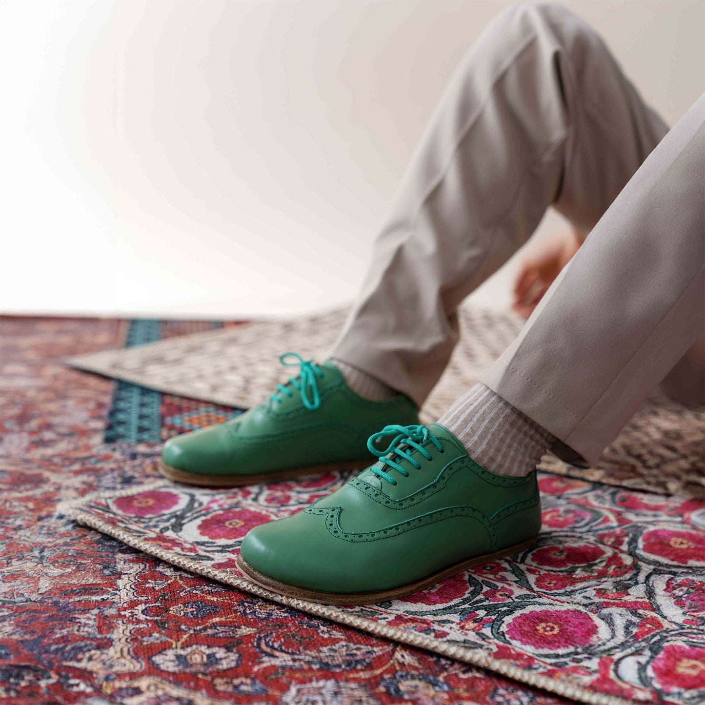 Man wearing green Doris barefoot Oxfords paired with beige pants on a patterned rug – modern look.