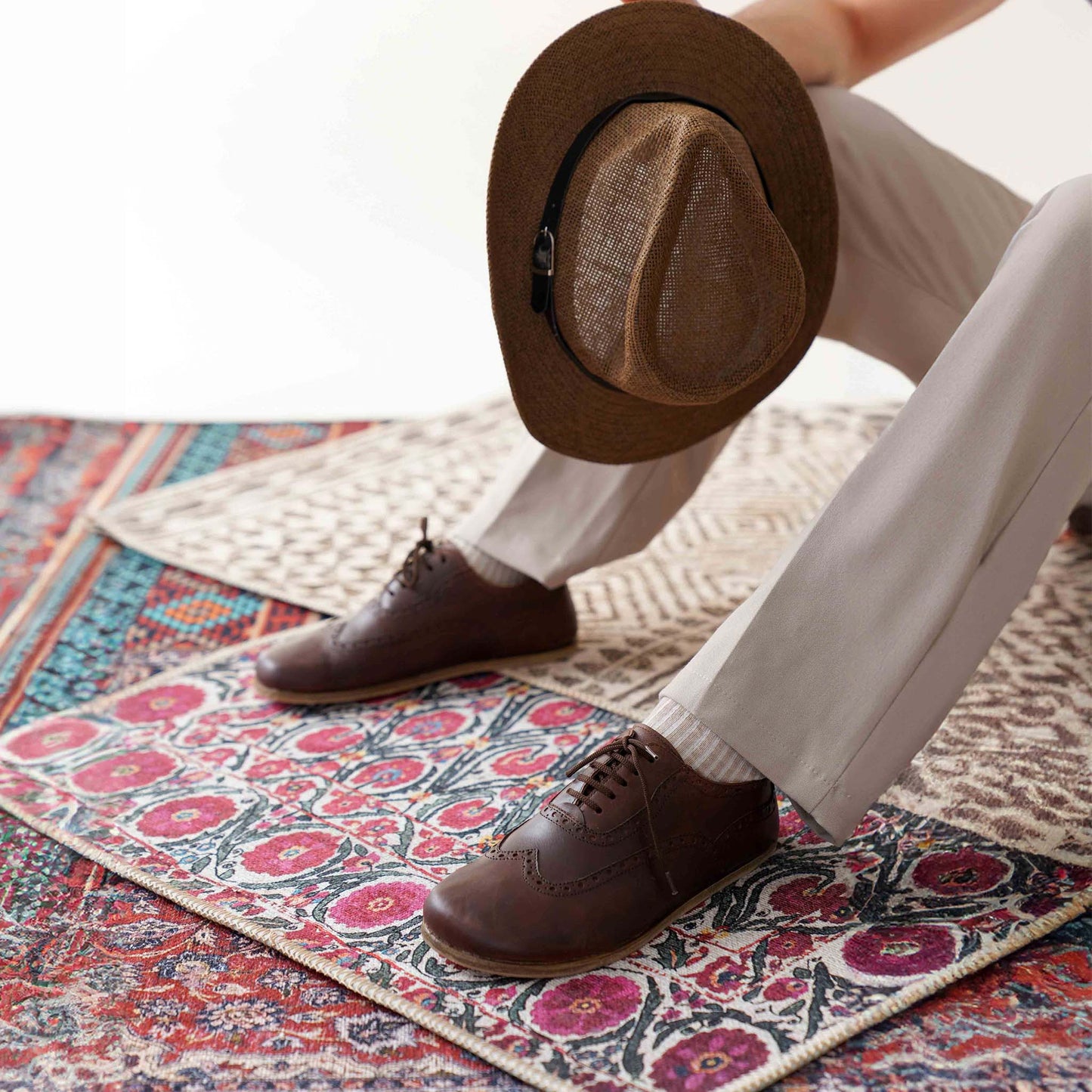 Man wearing brown Doris Leather Barefoot Men's Oxfords, sitting on a rug, showcasing their comfort and style.