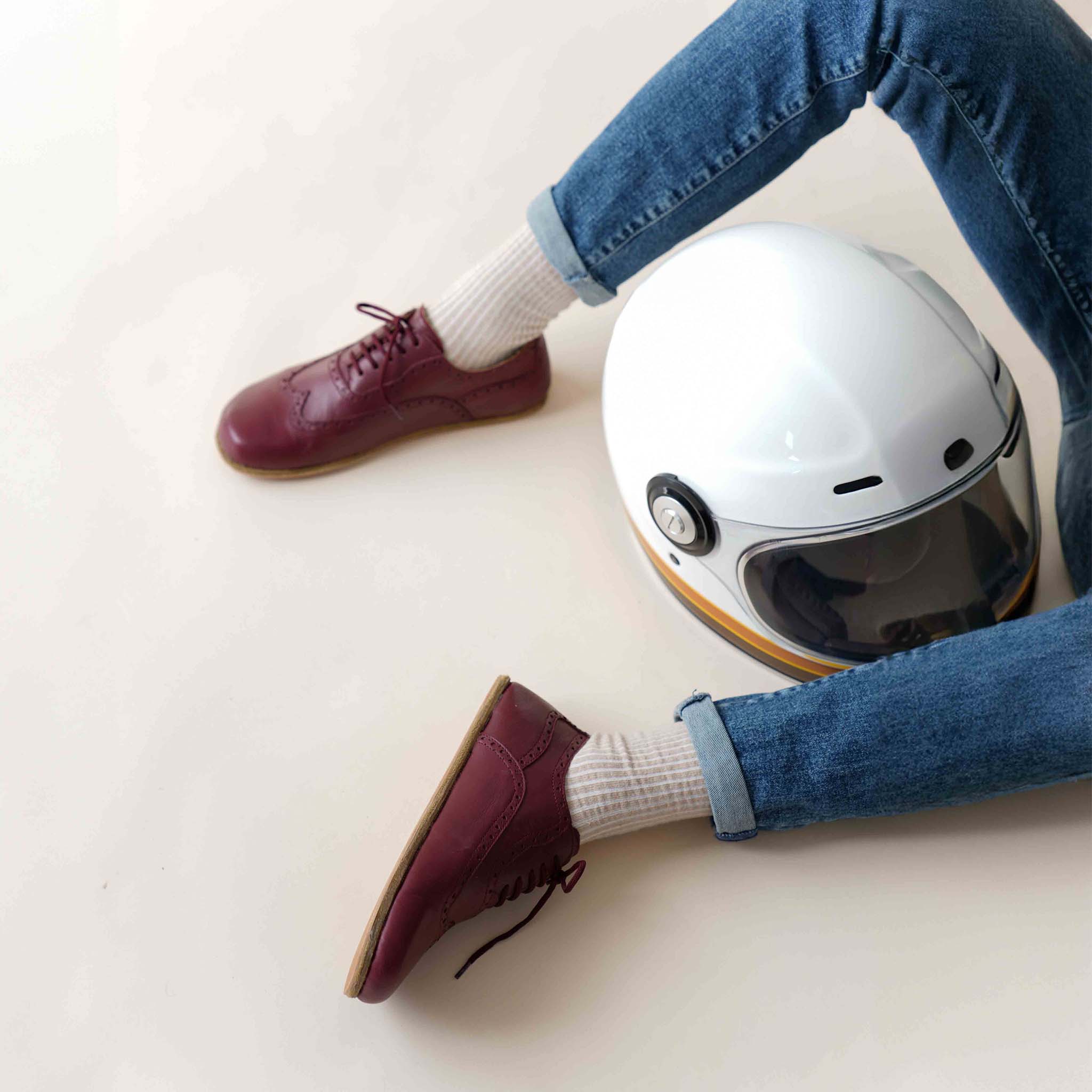 Man wearing burgundy barefoot Oxfords, paired with jeans and a white helmet – perfect casual look.