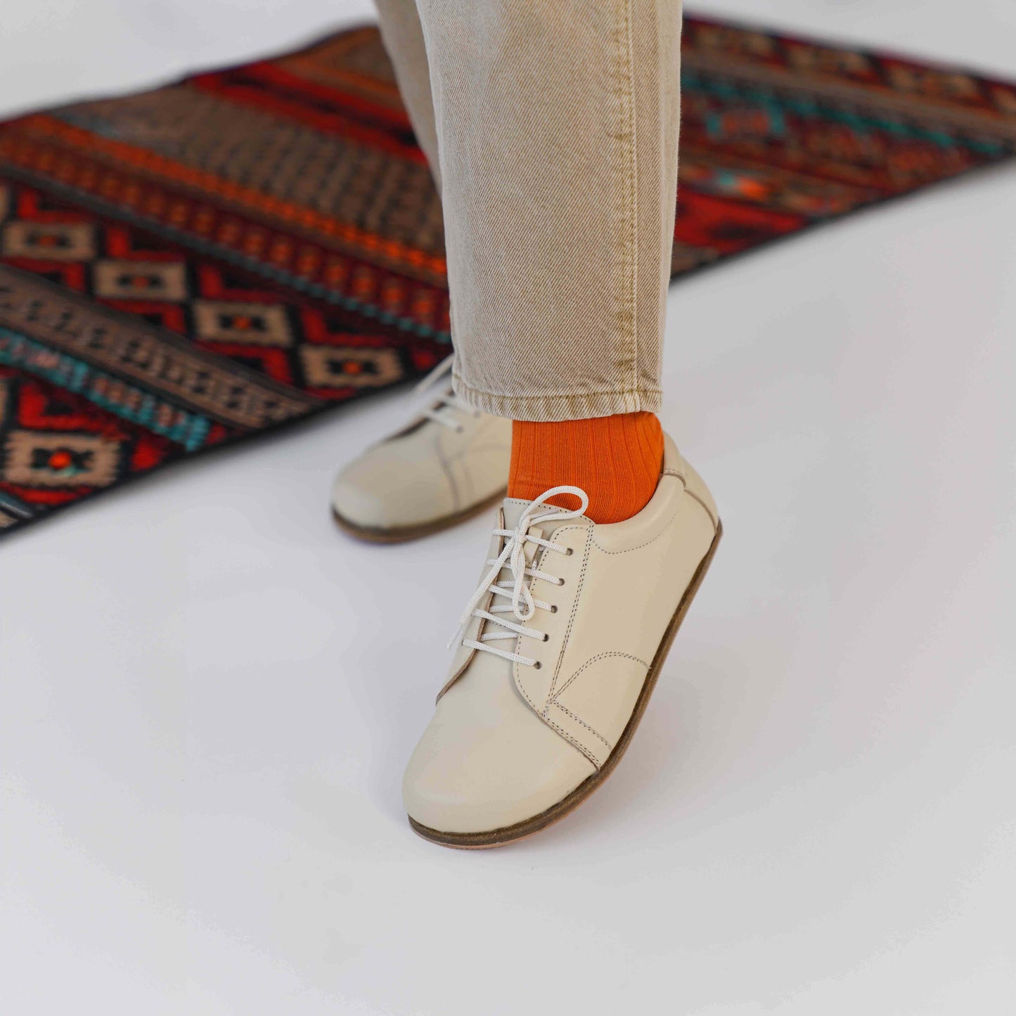 Beige leather barefoot women's sneakers in front of a rug, emphasizing the blend of traditional craftsmanship and modern style.