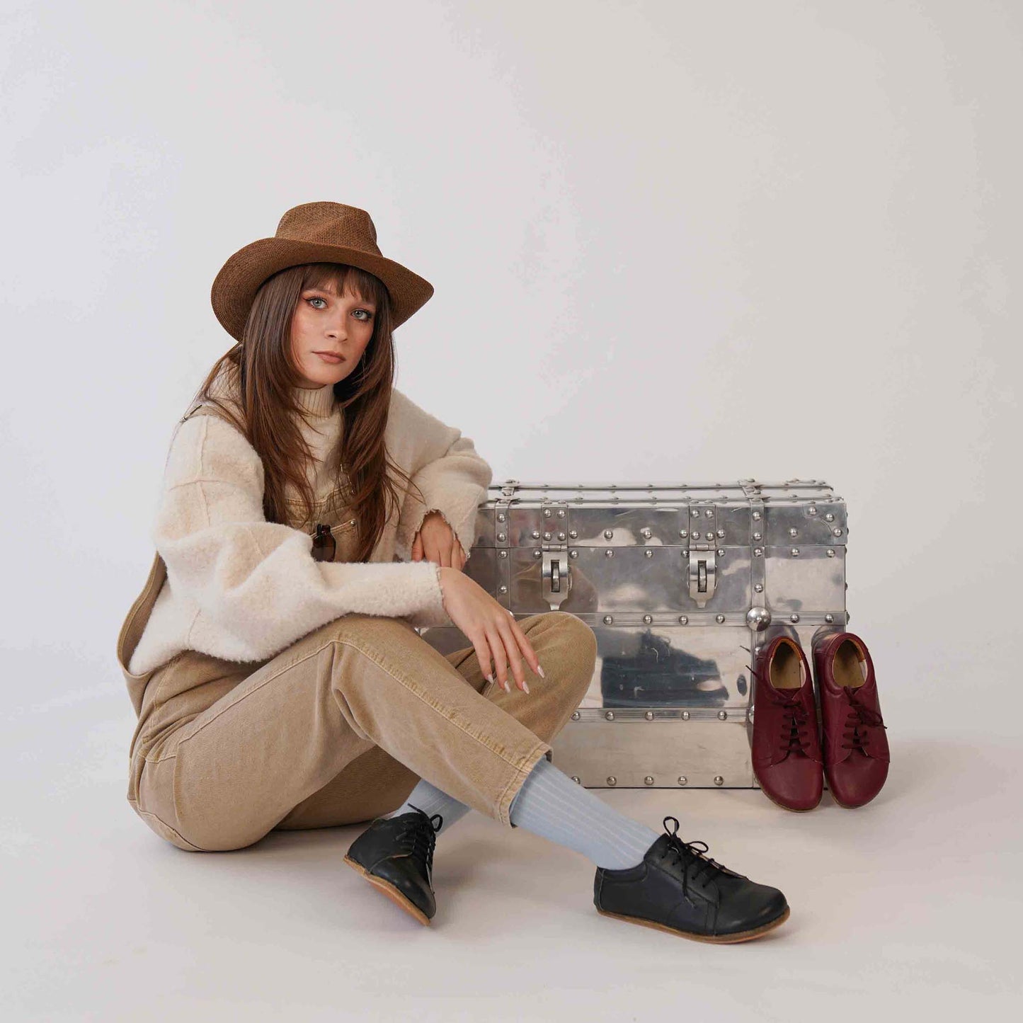 Model sitting next to a metal chest, wearing black Lydia Leather Barefoot Women's Sneakers, emphasizing their sleek design and comfortable fit.