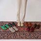 A model standing on a Persian rug wearing tan brown Lydia leather barefoot women's sneakers, emphasizing comfort and style.