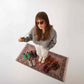 Top view of a model wearing Lydia Leather Barefoot Women Sneakers in brown, standing on a patterned rug with other shoe colors around.