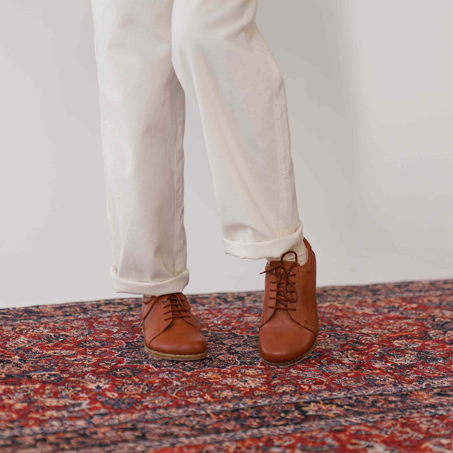 A close-up of a model's feet wearing tan brown Lydia leather barefoot women's sneakers, highlighting the minimalist design and natural fit.