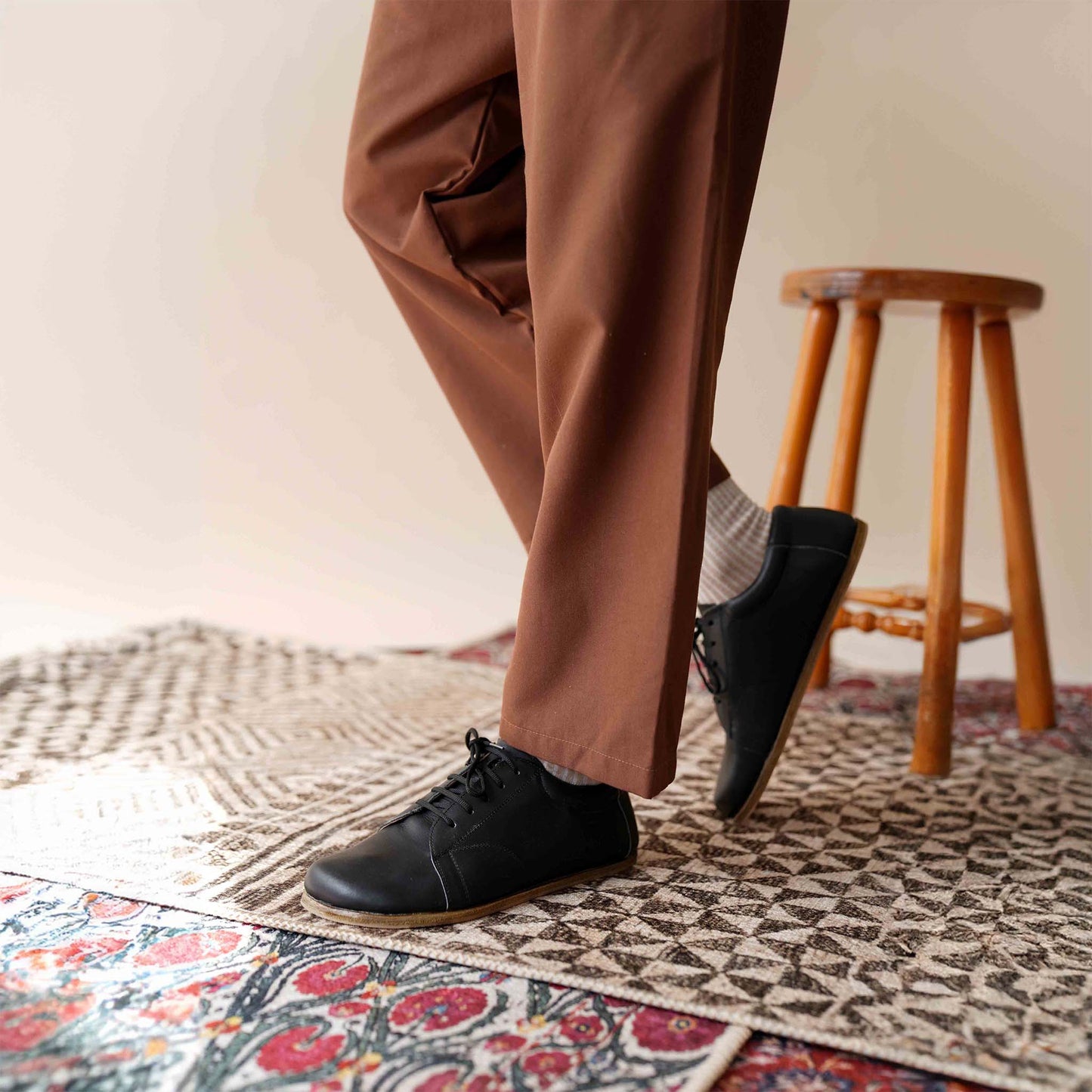 Close-up of a model's feet wearing Black Lydia Leather Barefoot Men's Sneakers, standing on a decorative rug.